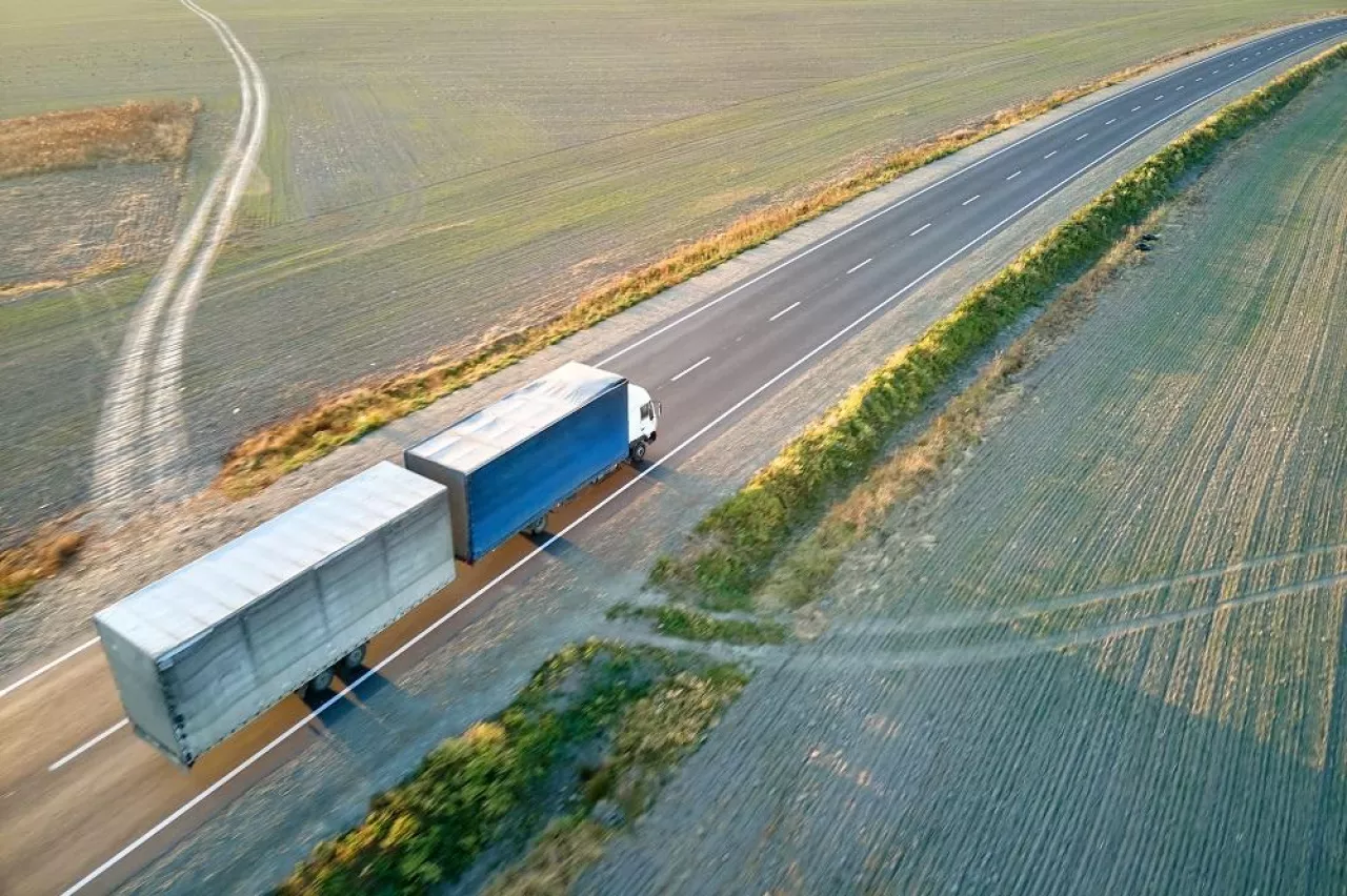 Aerial view of blurred fast moving semi-truck with cargo trailer driving on highway hauling goods in evening. Delivery transportation and logistics concept.