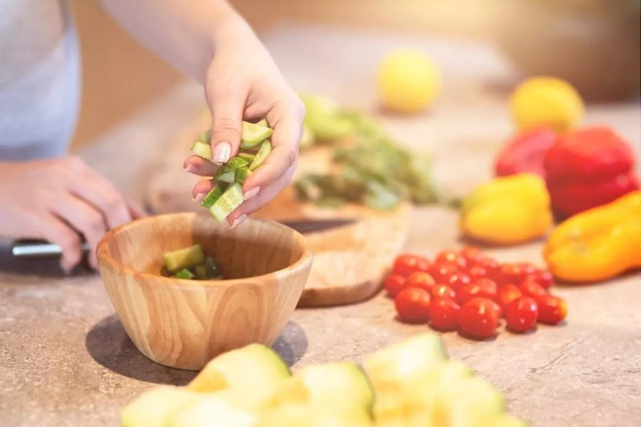 Close up shot of female hand putting ingredients for a salad in a bowl. Daily menu for pregnant woman. Horizontal shot. Selective focus
