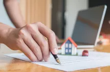 Pen handles signed documents with model houses, model car and laptop on the table.