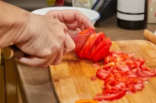 Woman cuts tomatoes for cooking at home using recipe from the Internet. Preparation of ingredients and vegetables before cooking.
