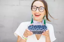 Portrait of a young smiling woman standing with bluberries on the gray wall background