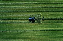 Blue tractor mowing green field, aerial view. Drone photo