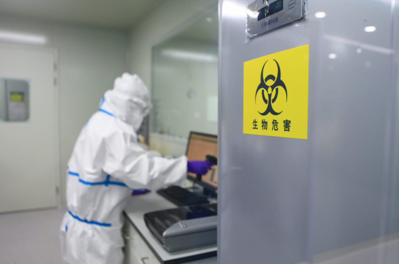 Pracownik w kombinezonie ochronnym pracuje w laboratorium oznaczonym symbolem zagrożenia biologicznego (zdjęcie poglądowe)