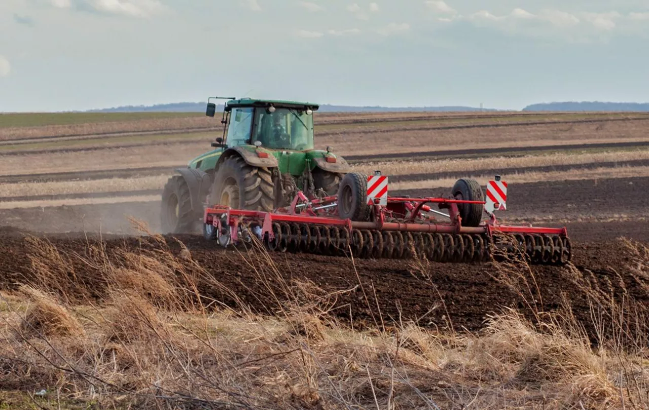 Widok na ciągnik z kultywatorem przedsiewnym pracujący na polu uprawnym wczesną wiosną.