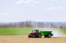 Ciągnik rolniczy z rozsiewaczem dwutarczowym wirnikowym podczas wiosennej aplikacji nawozów mineralnych na polu.