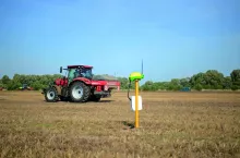 Ciągnik z zaczepionym rozsiewaczem nawozów jedzie na polu, na pierwszym planie widoczna jest antena GPS